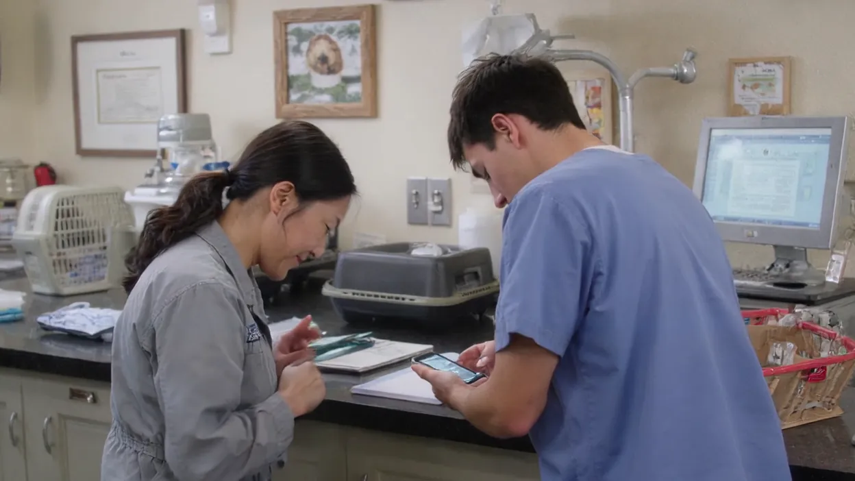 A practice manager shows a new hire something on his phone at a counter in a veterinary office.