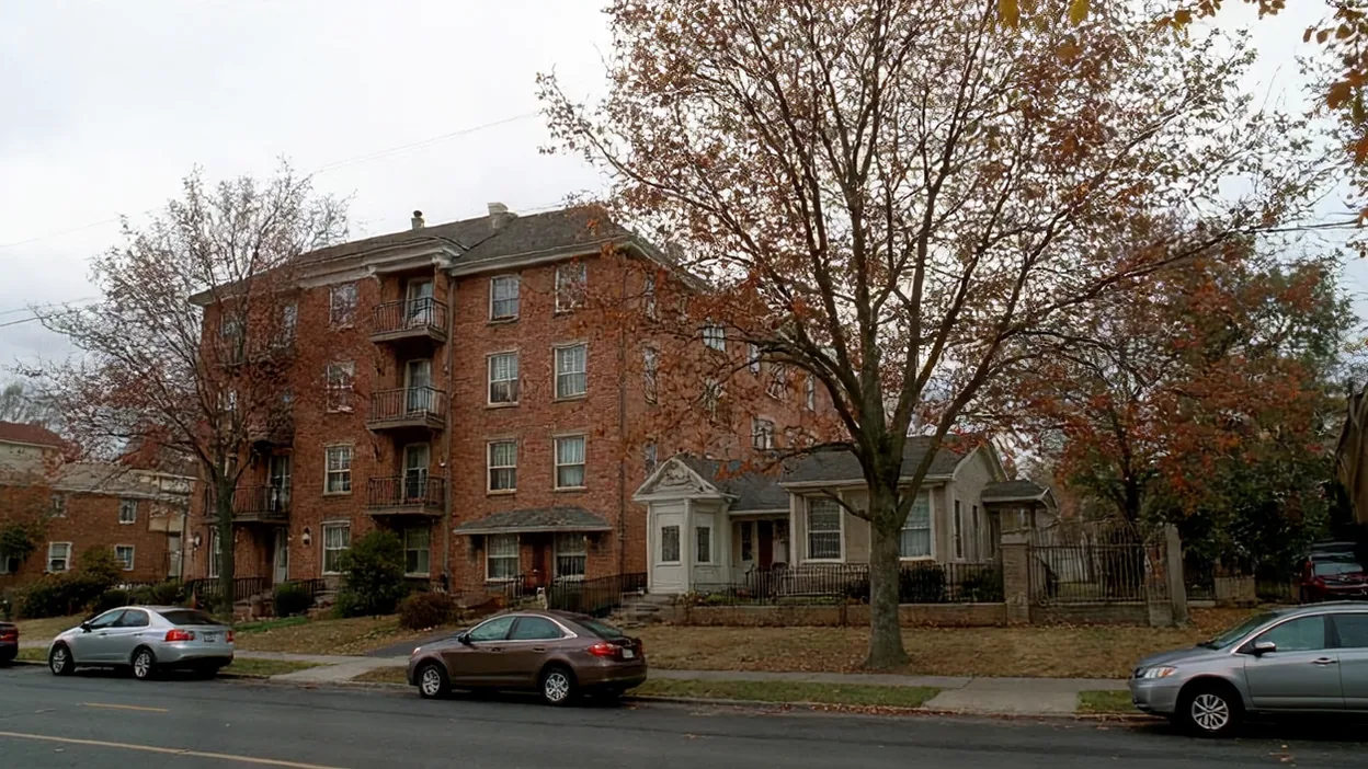An apartment building and a small single-family house side by side on a tree-lined street in autumn.
